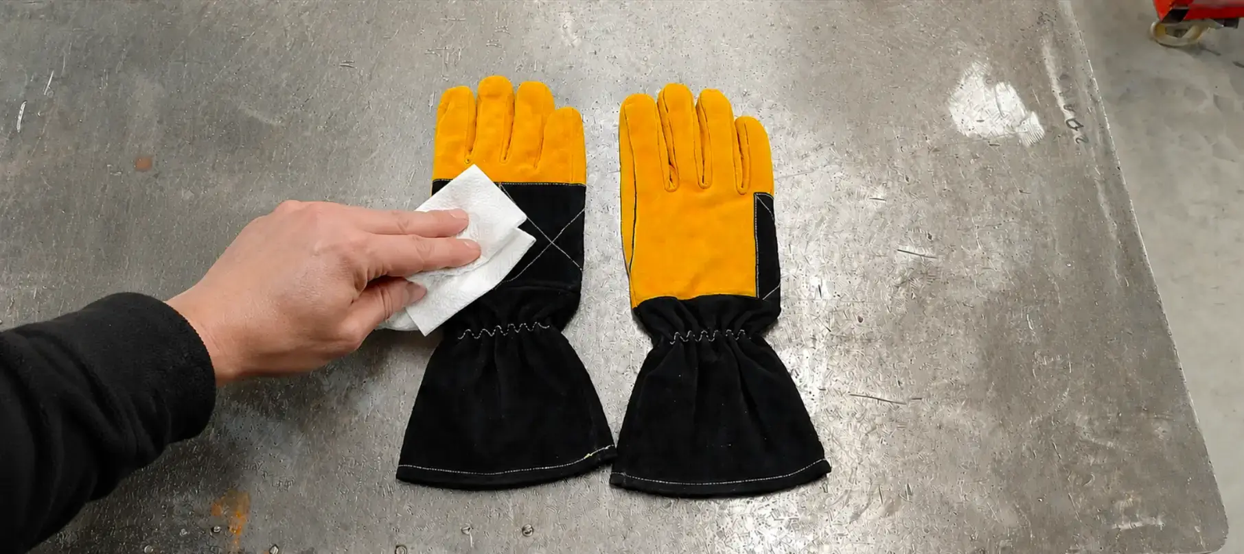 Cleaning ARASWELD leather welding gloves with a soft cloth to remove dust, welding residue, and surface contaminants before conditioning and routine maintenance.