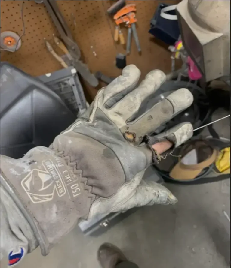 Old welding glove with torn fingertips and damaged leather showing signs of excessive wear.